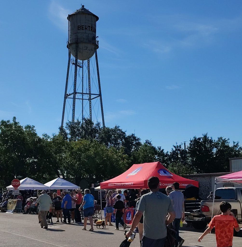 Crowds browse vendor booths at the Oatmeal Festival in Bertram, Texas, with the iconic Bertram water tower in the background