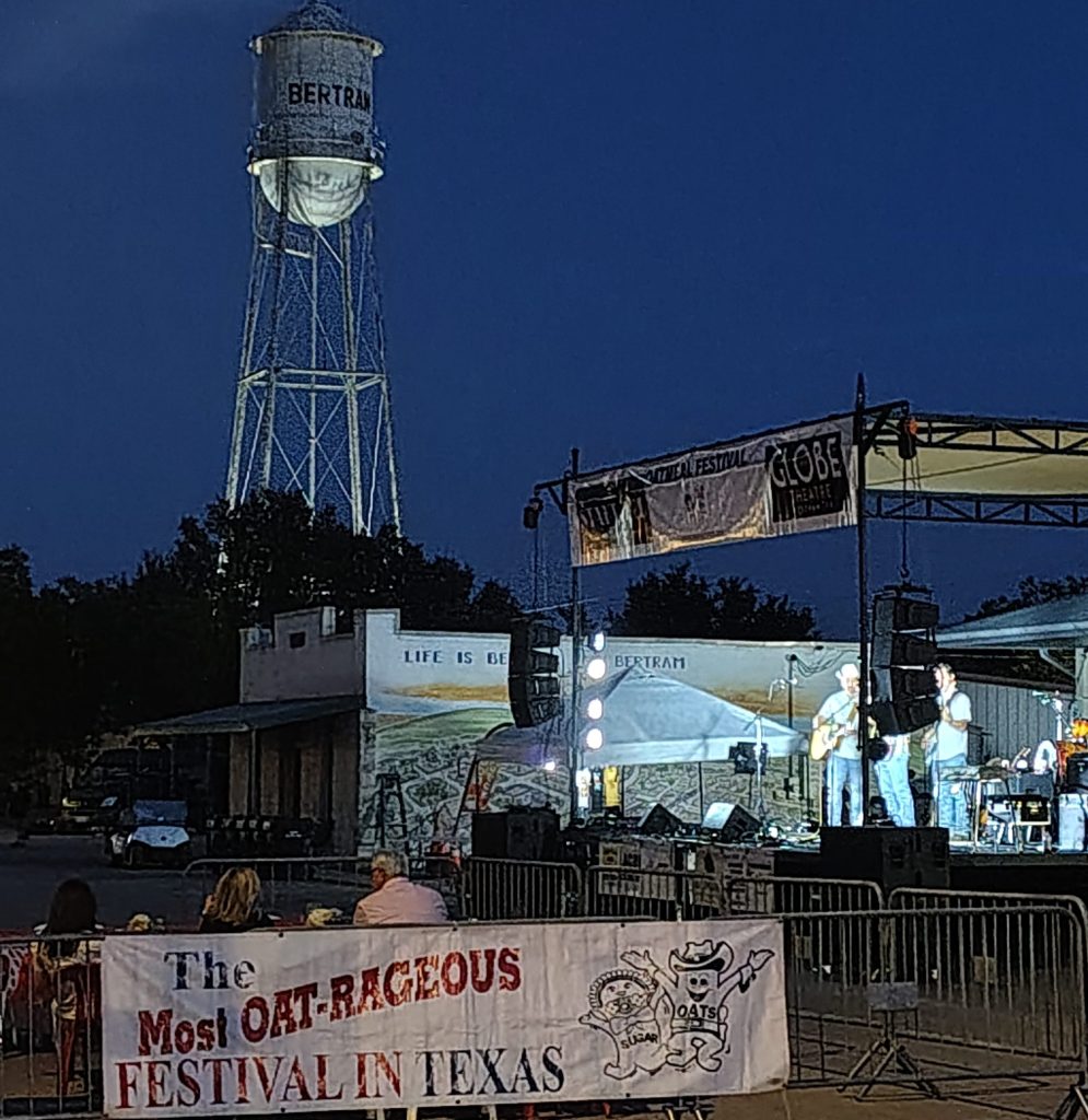 Live music on stage at the Oatmeal Festival street dance in Bertram, Texas, with the illuminated Bertram water tower in the background